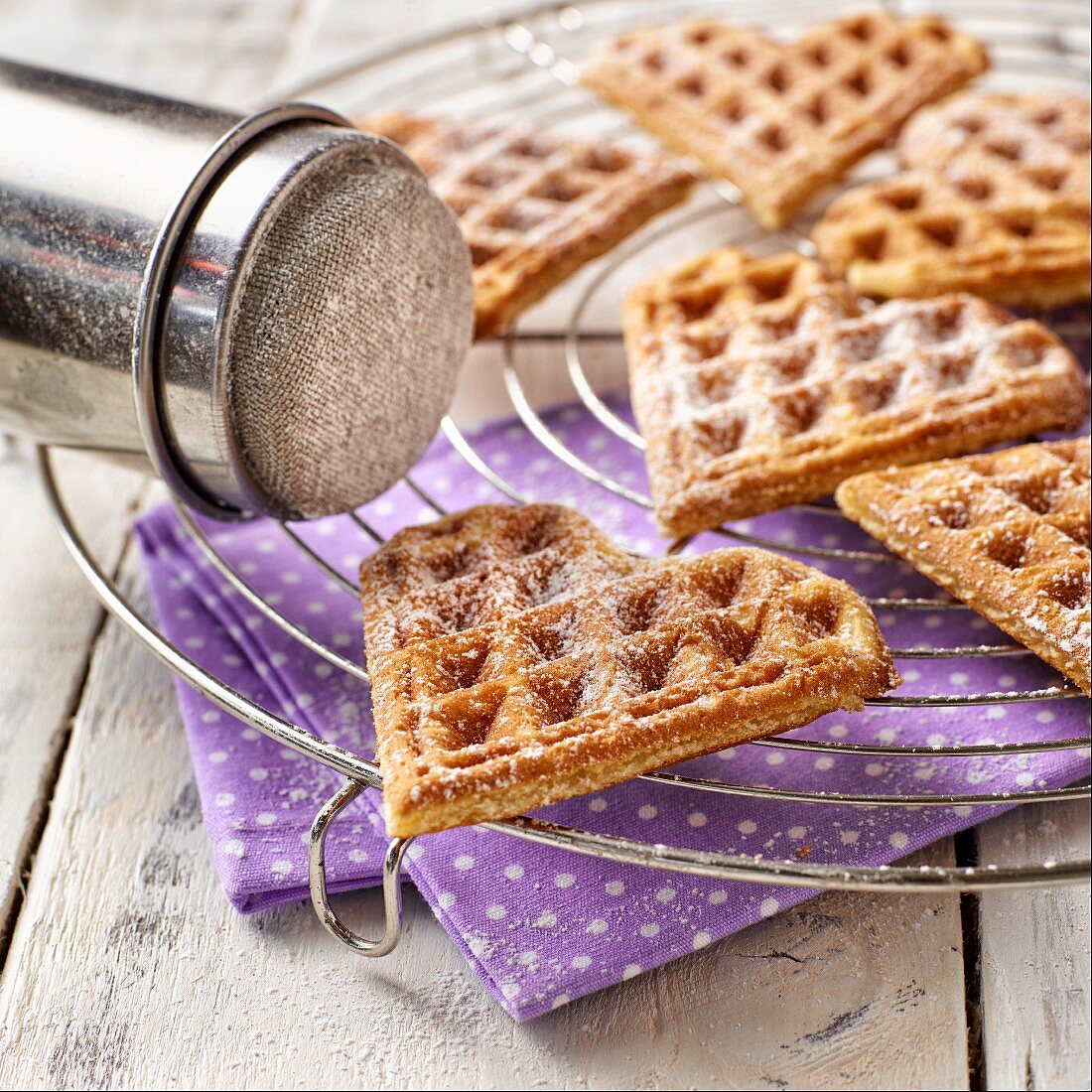 Heart-shaped waffles dusted with icing sugar on a wire rack