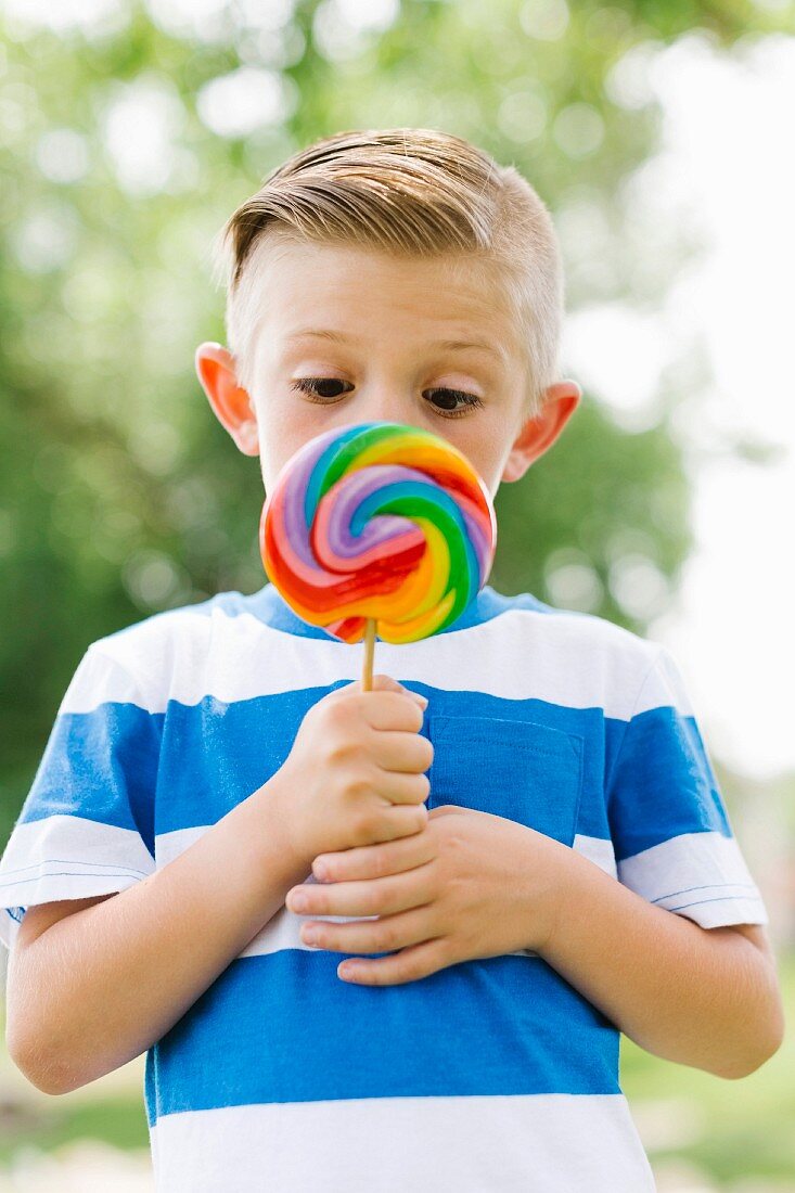 Boy squinting and holding big, colorful lollipop