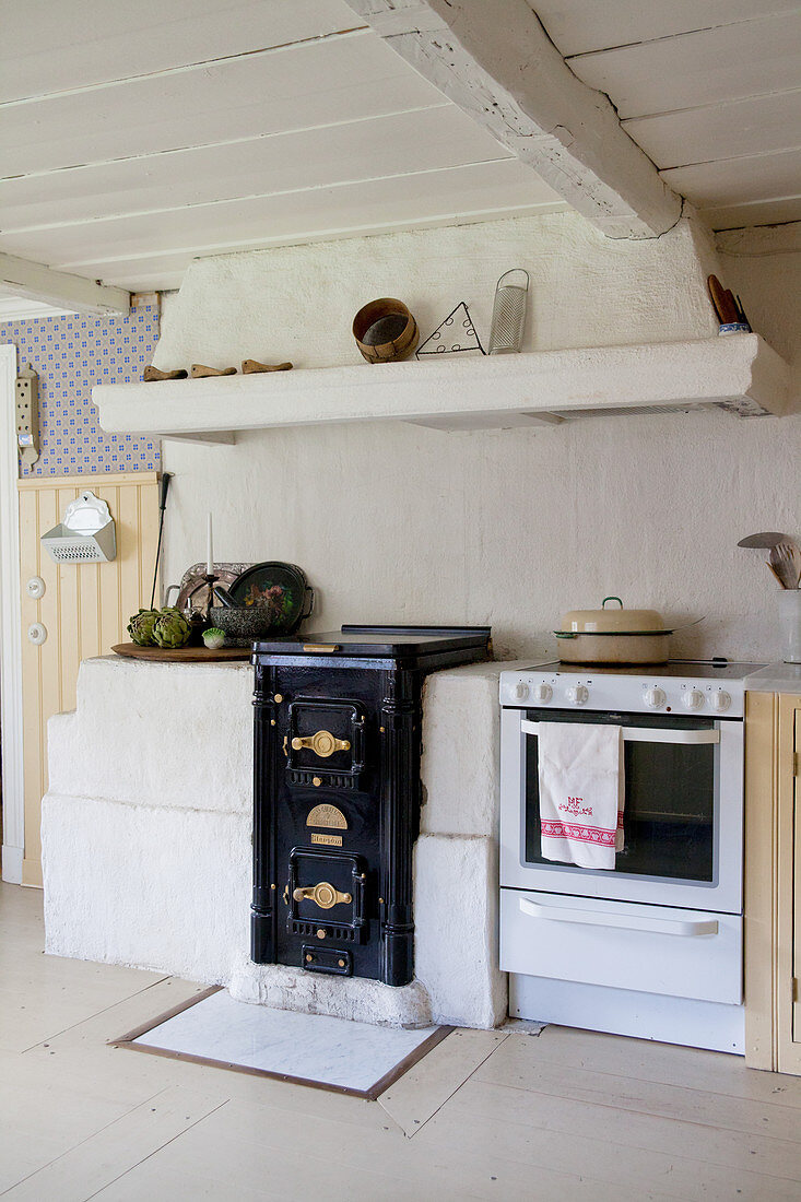 Cooker and old wood-fired stove below extractor hood in country-house kitchen