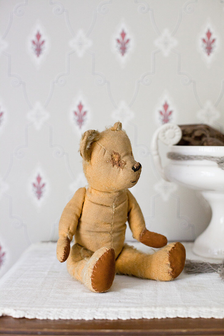 Alter geflickter Teddybär vor nostalgischer Tapete