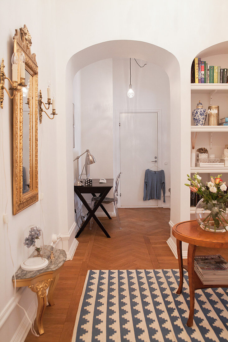 Baroque console table and gilt-framed mirror in classic hallway with arched doorway