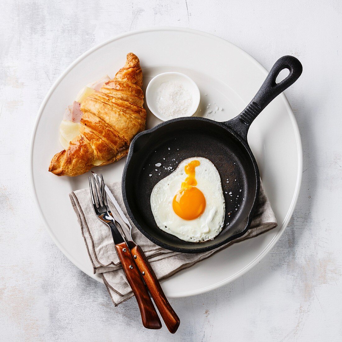 Breakfast with Fried egg on iron pan and croissant sandwich with cheese and ham on white plate on white background