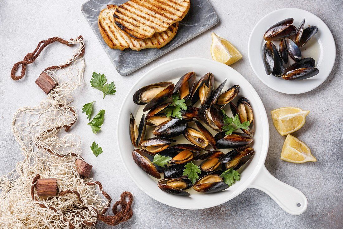 Mussels in cooking pan with parsley, toasted bread and fishnet on white background