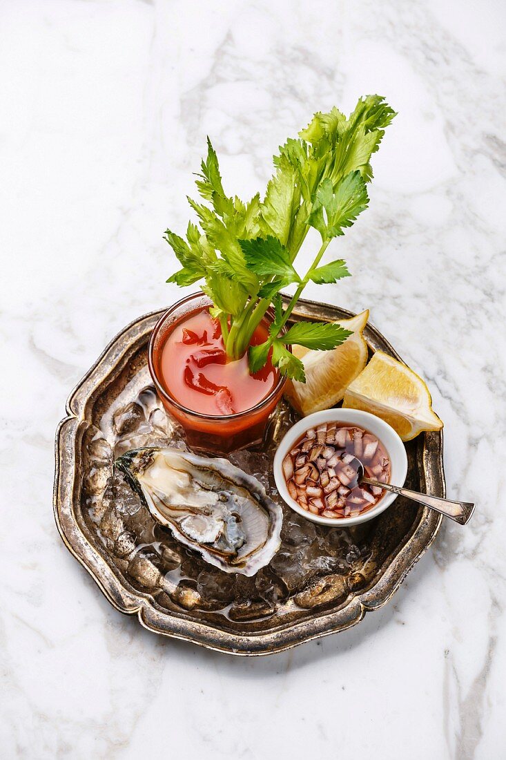 Open Oyster Fines de Claire and Bloody Mary cocktail on white marble background