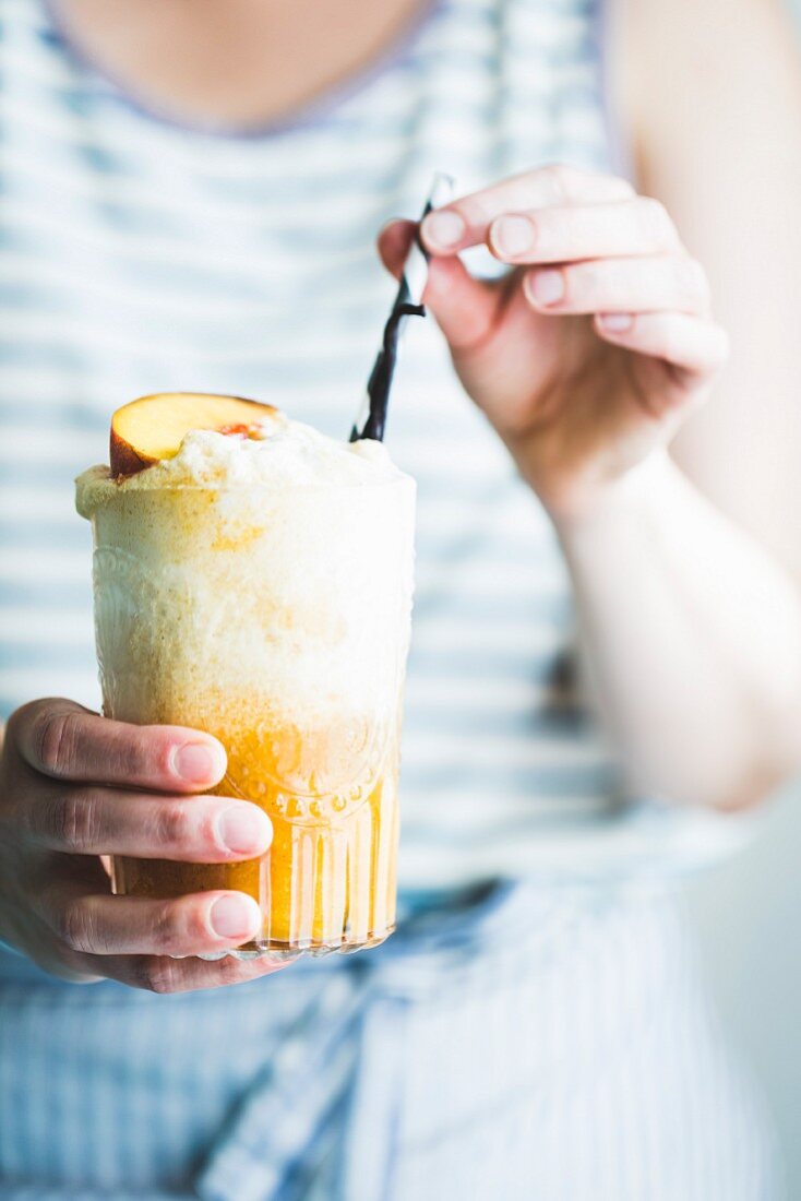 Frau hält ein Glas Pfirsich-Float (Getränk mit Eiscreme und Früchten)