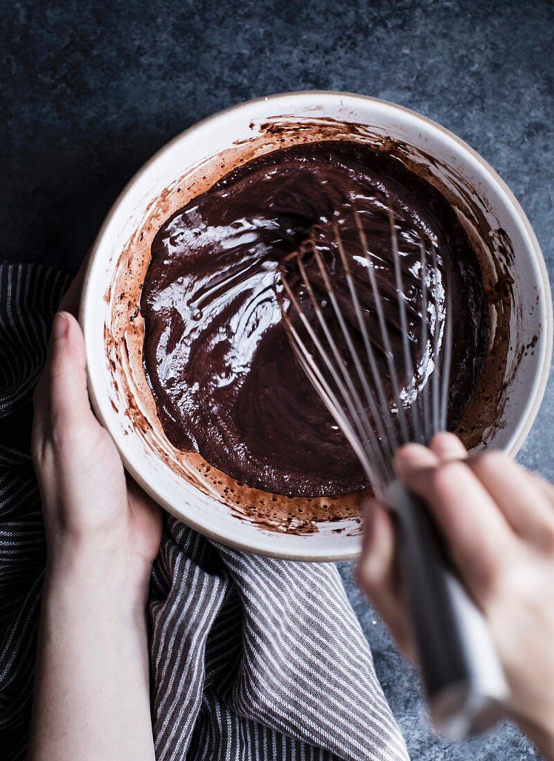 A womans hand whisking chocolate sauce in a bowl
