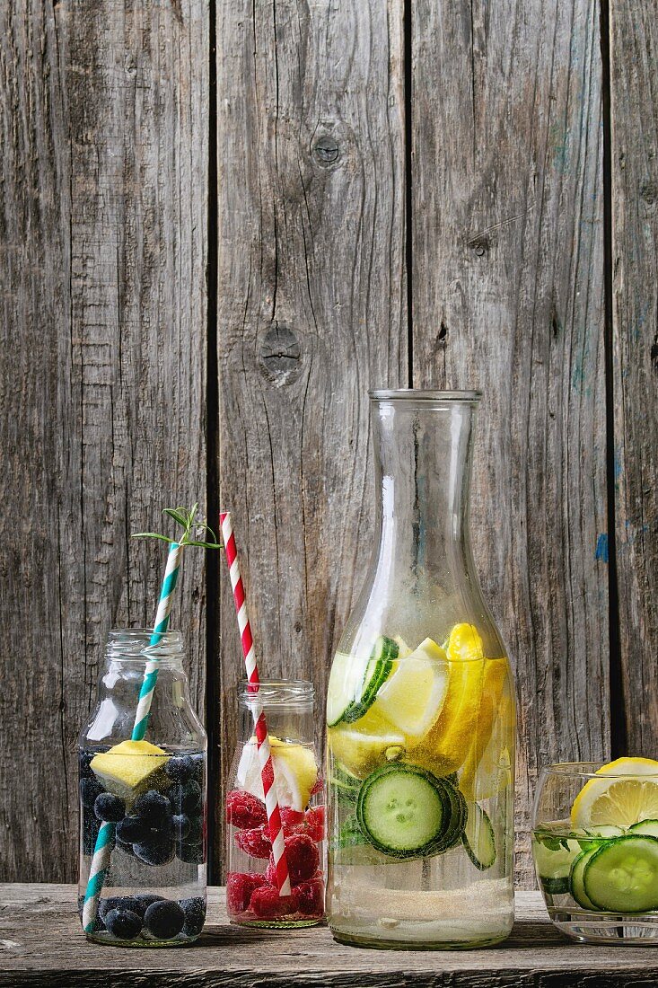 Citrus cucumber berries blueberry and rasberry sassy sassi water for detox in glass bottles with cocktail tubes on wooden background