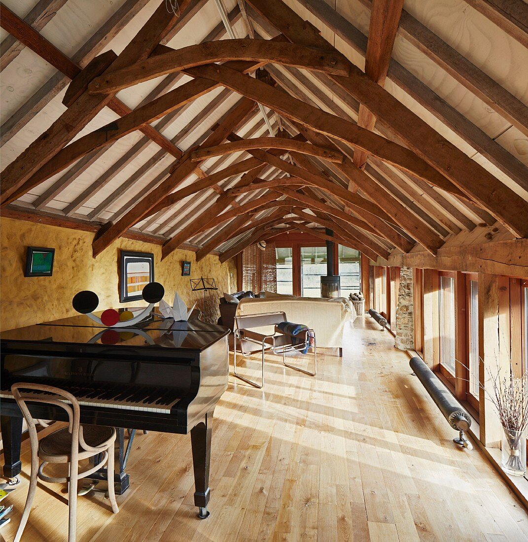 Grand piano in bright room in rustic attic with restored wooden roof structure