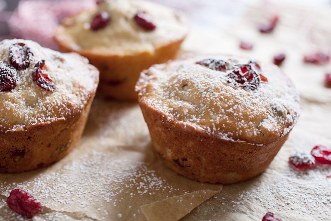 Freshly baked cranberry muffins on parchment paper with sugar icing
