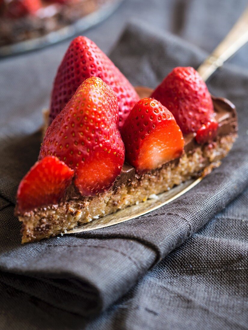 Slice of gluten free chocolate tart served with fresh strawberries