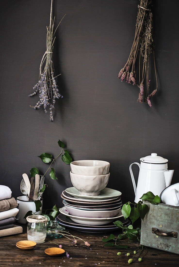 Vintage-Küchenutensilien auf Holztisch vor grauer Wand mit Trockenblumen