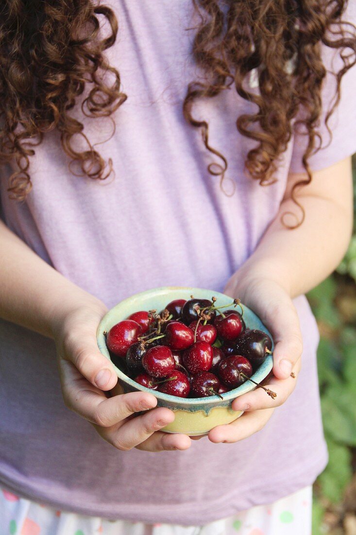 A young girl holding a bowl of fresh cherries