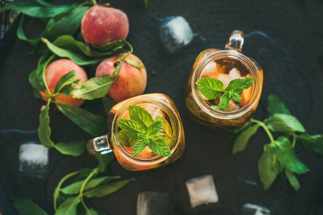 Summer refreshing cold peach ice tea with fresh mint in glass jars on metal tray background
