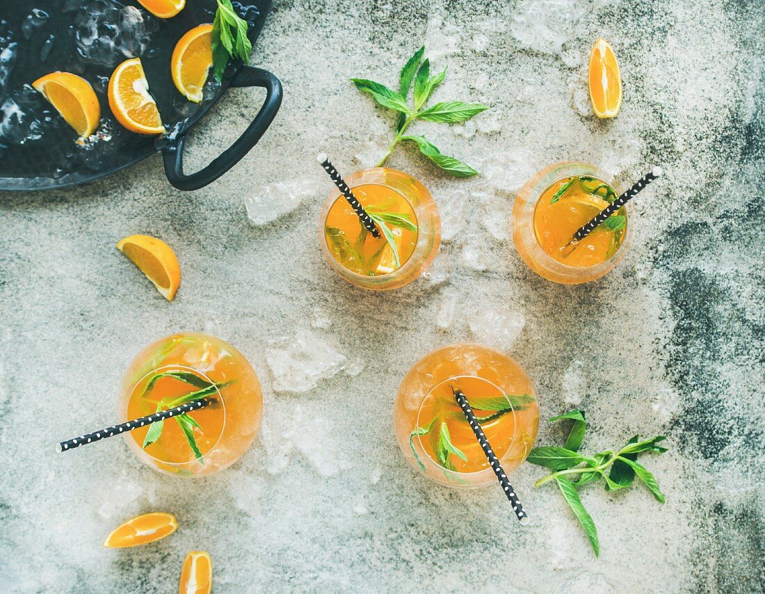 Erfrischender Sommercocktail mit Orangen, Pfefferminze und Crushed Ice in Gläsern (Aufsicht)