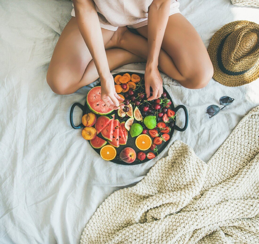 Young girl wearing pastel colored home clothes taking cherries from tray full of fresh seasonal fruit