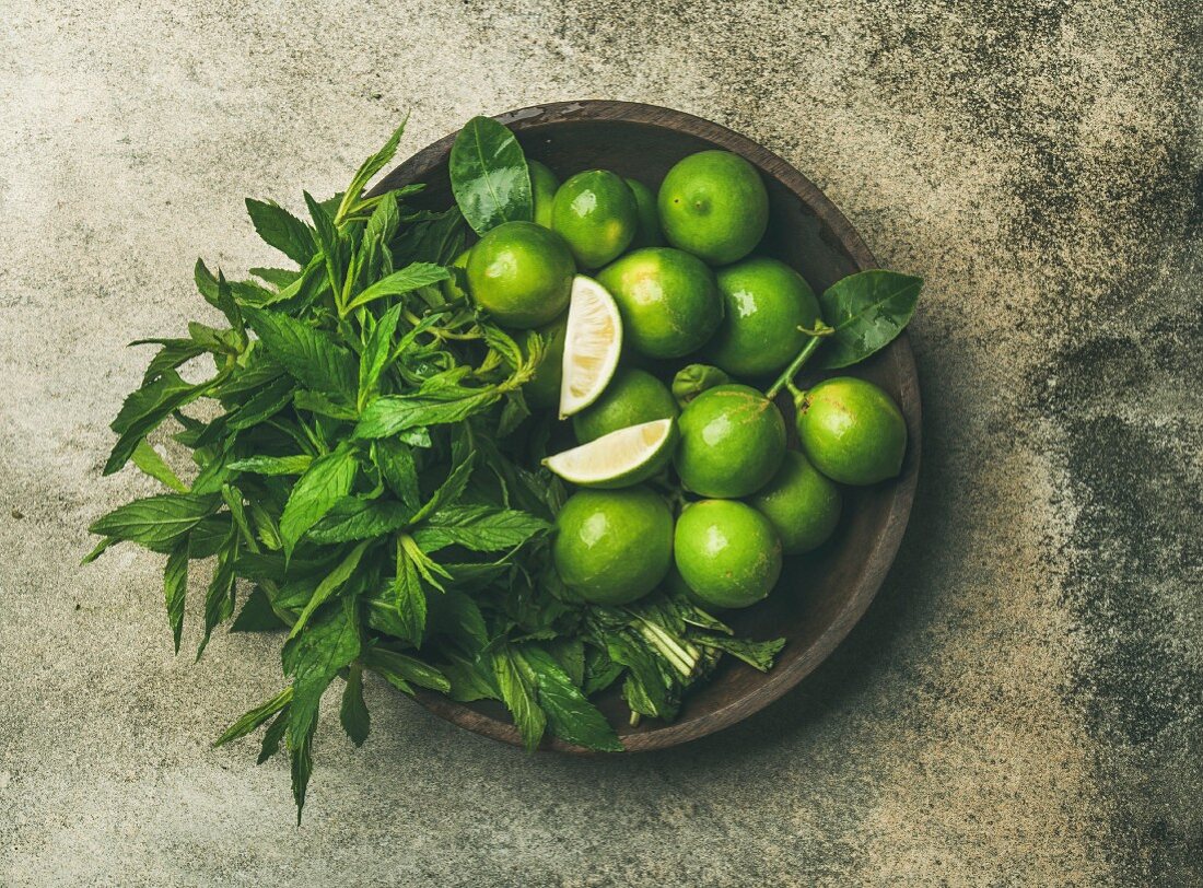 Flatlay of freshly picked organic limes and mint leaves for making cocktail or lemonade in wooden plate