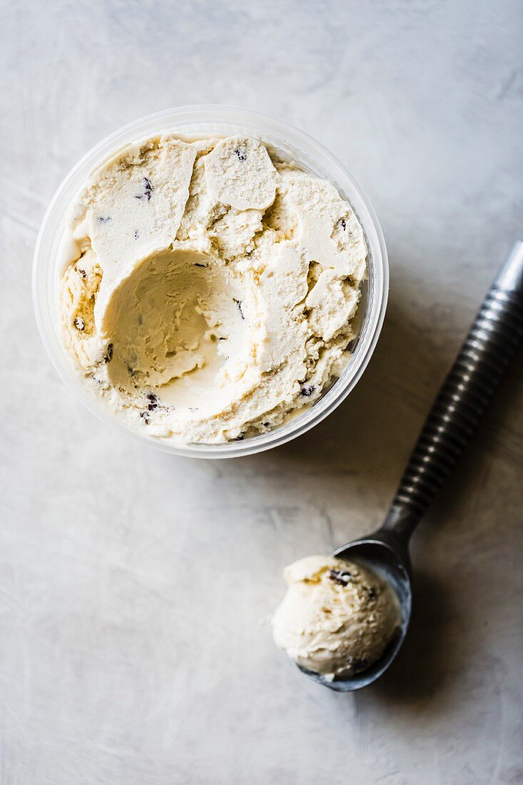 Chocolate-Chip-Eiscreme in Plastikgefäss und Eisportionierer (Aufsicht)