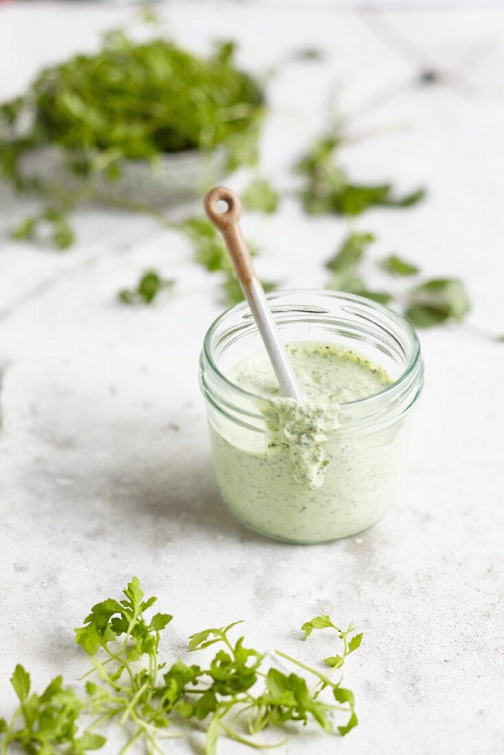 Green sauce in a glass surrounded by fresh herbs