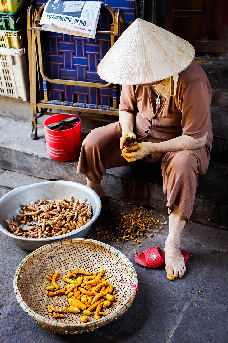 A woman peeling fresh turmeric in Hoi An, Vietnam