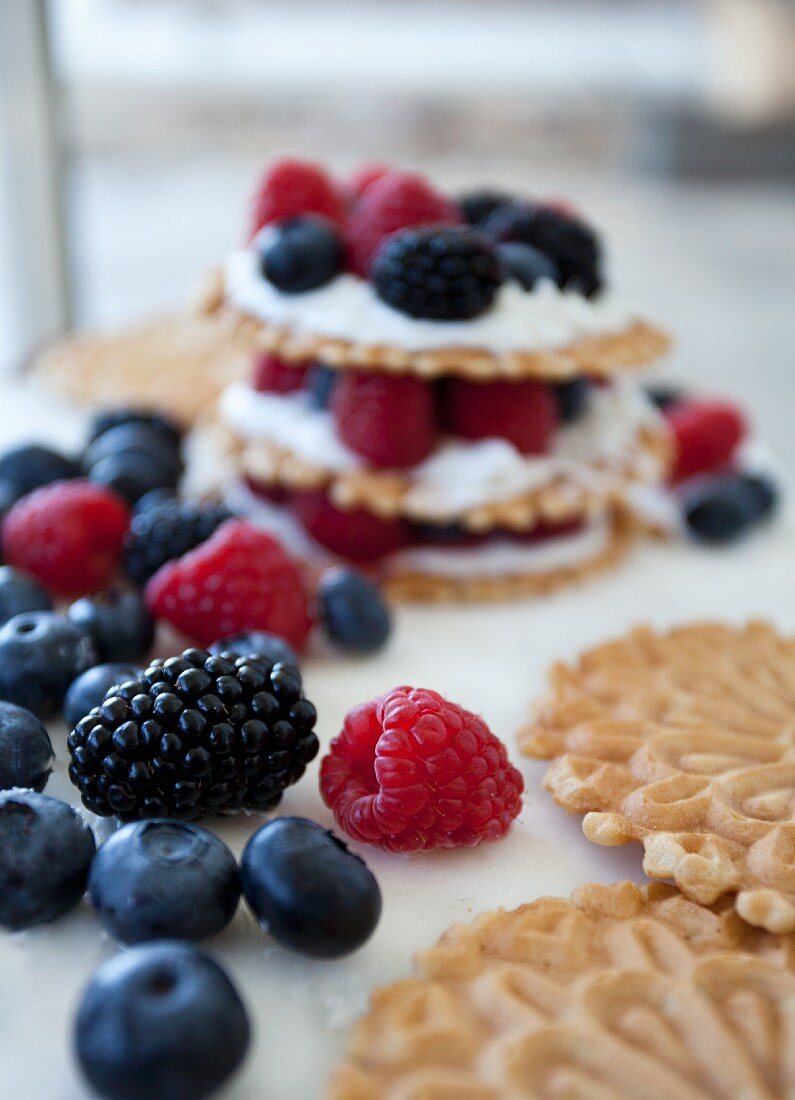 Stacks of wafer cookies, icing and mixed berries with a white background