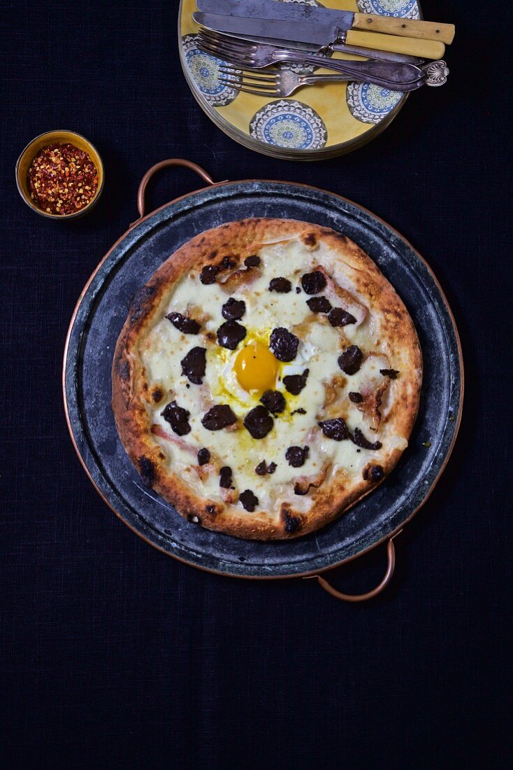 Pizza mit Ei und schwarzen Trüffeln auf Keramikteller (Aufsicht)
