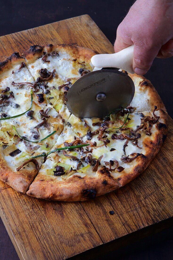 Pizza bianca with mushrooms and leek being cut with a pizza cutter