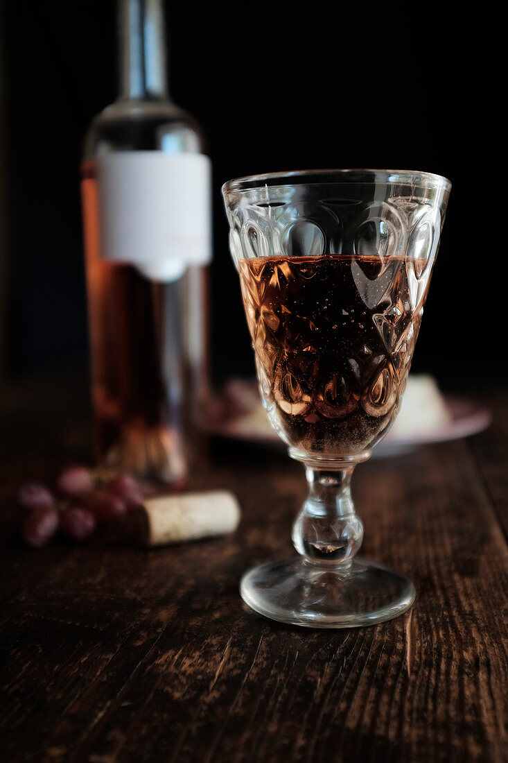 Flasche und Glas Rosewein auf rustikalem Holztisch