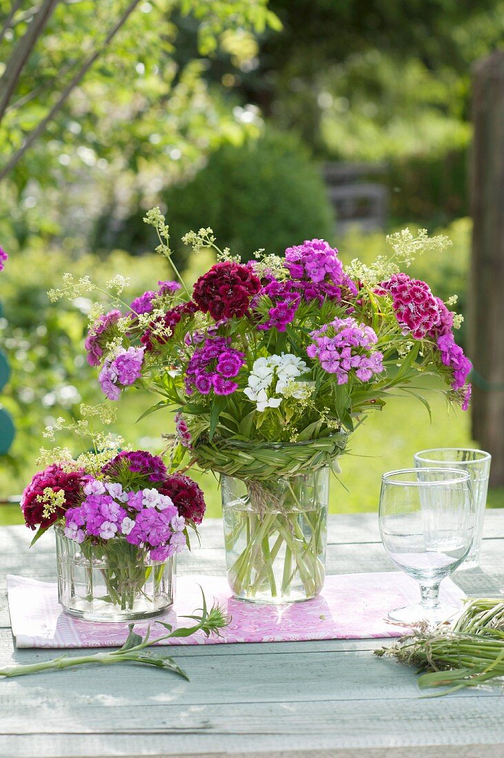 Bouquets of Dianthus barbatus (sweet William) and Galium verum (lady's bedstraw) with plaits of glass tied around jars