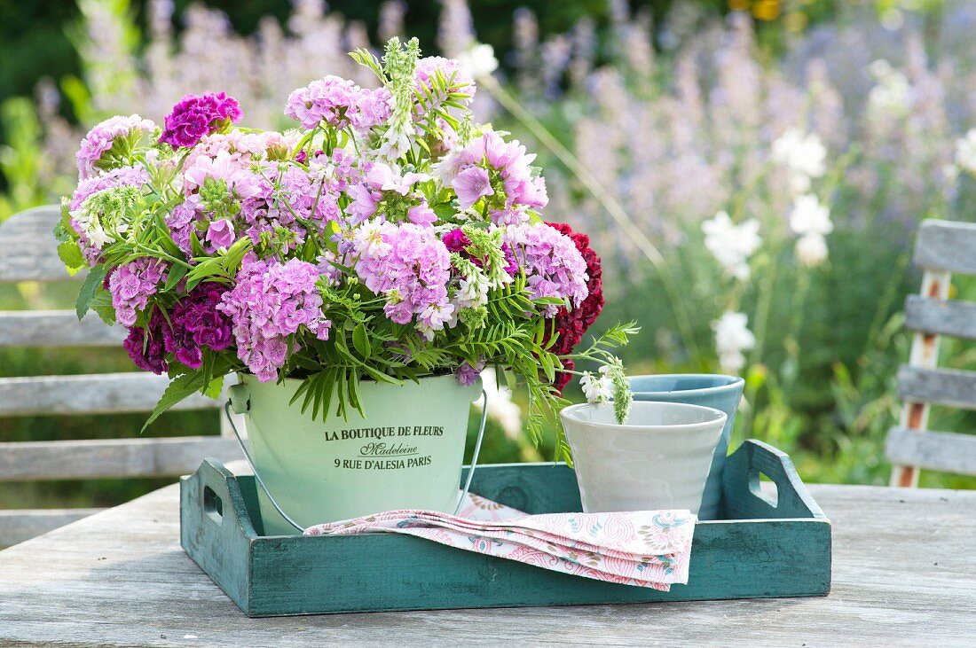 Ländlicher Strauß aus Dianthus barbatus (Bartnelke), Galega (Geißraute) und Malva moschata (Moschus - Malve) in Blecheimerchen auf Holz-Tablett