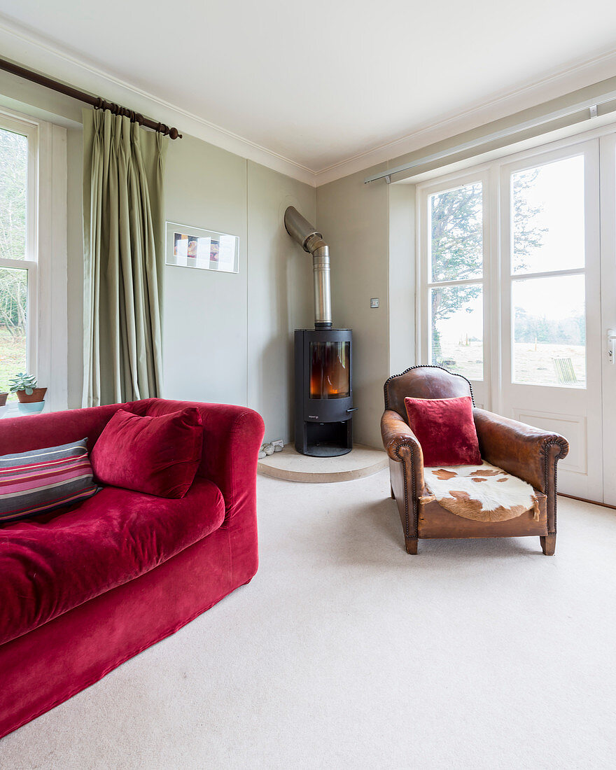 Old leather armchair and red sofa in front of wood-burning stove in corner