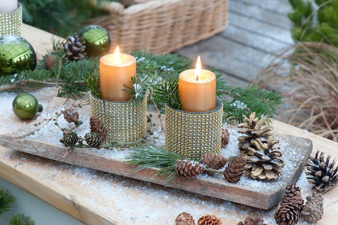 Candle decoration in goblets with gold decor on wooden board in the first snow
