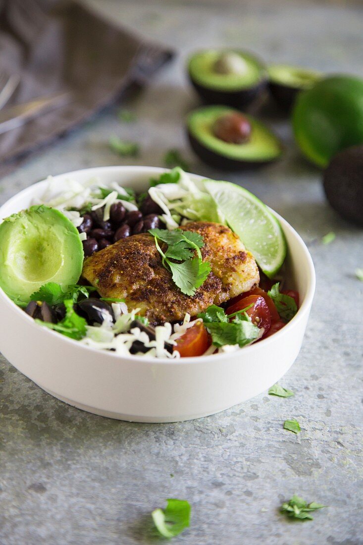 A taco bowl with fish, avocado, black beans, and white cabbage