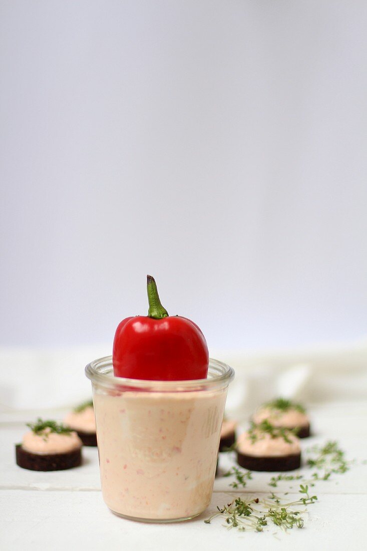 Red pepper spread in a glass and on pumpernickel disks