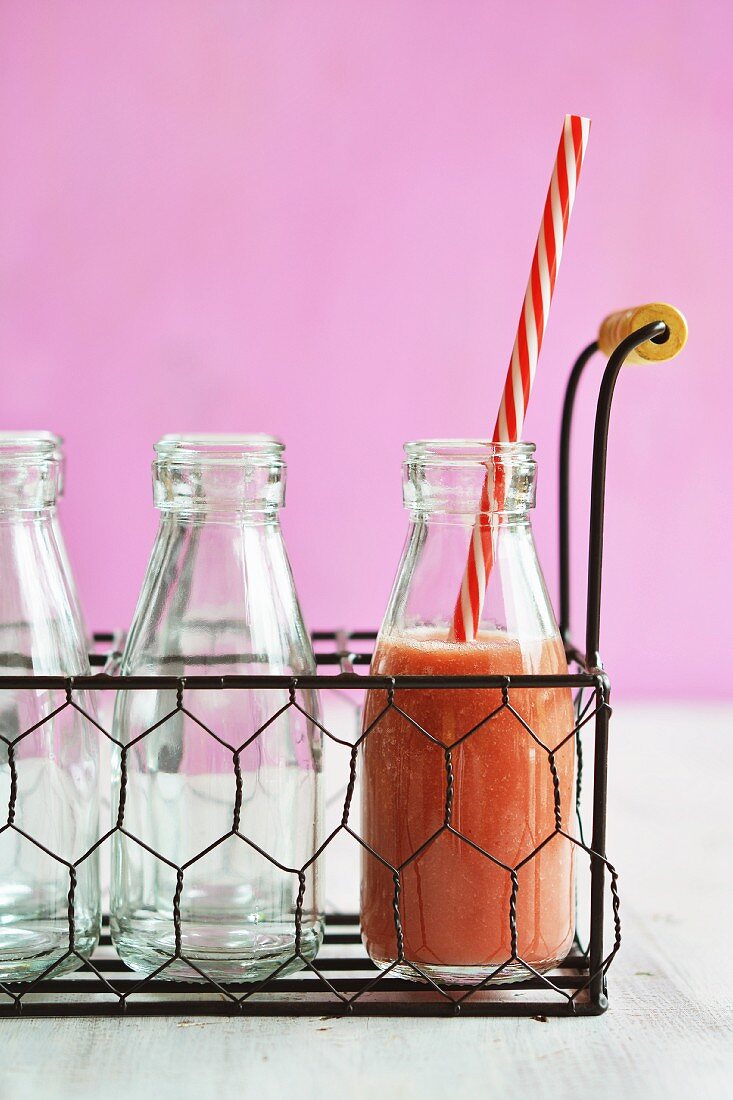 A bottle of watermelon smoothie with a straw in a wire basket