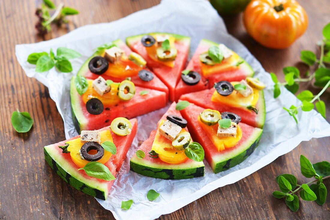Melonenstücke garniert wie eine Pizza mit Tomaten, Tofu, Oliven und frischen Kräutern