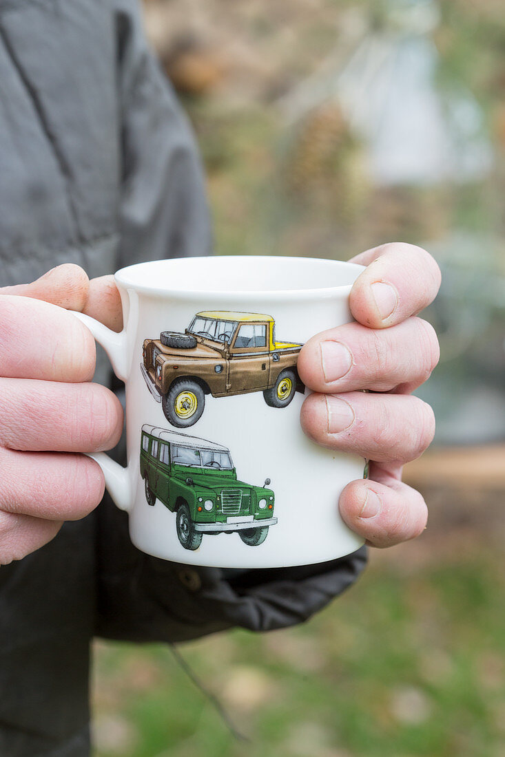 Hands holding mug with car motifs