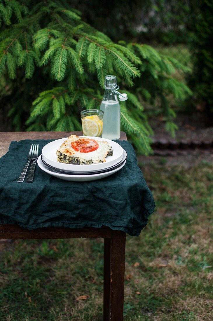 A slice of spinach lasagne served with lemonade on a table outdoors