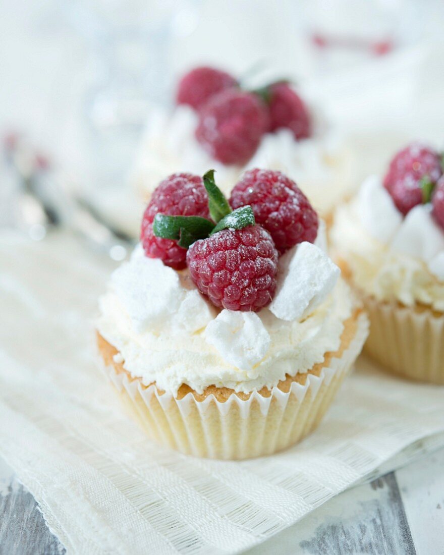 Cupcakes verziert mit Sahne, Baiserstückchen und Himbeeren