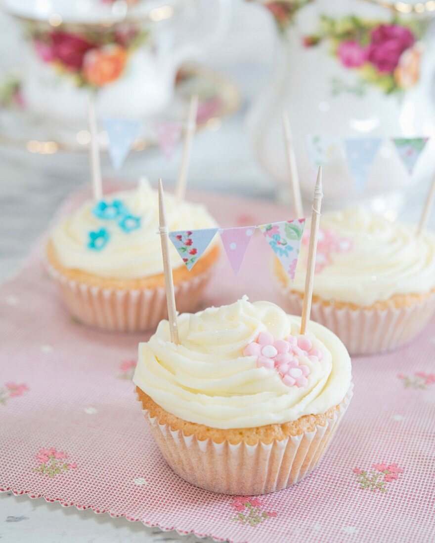 Cupcakes verziert mit Cremehäubchen, Zuckerblumen und Mini-Wimpelkette