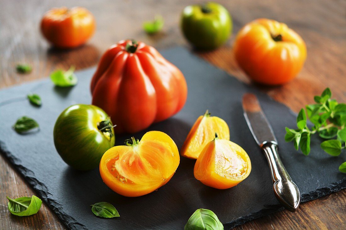 Colourful rustic tomatoes on a chopping board with an old knife and various herbs