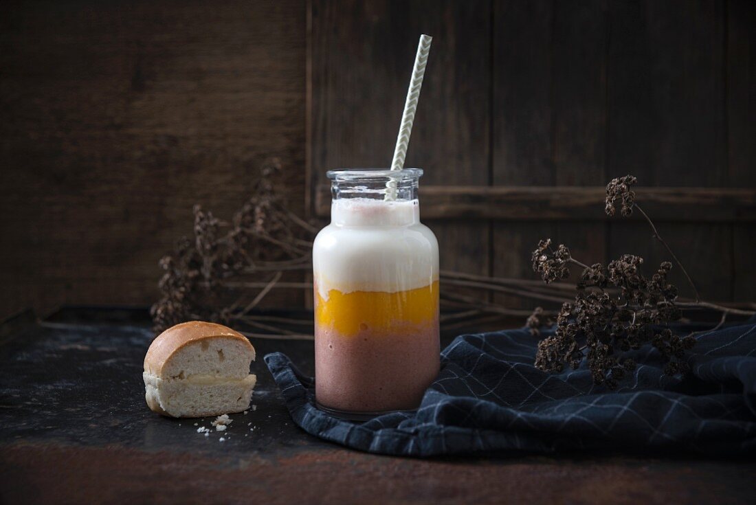 A tri-coloured soy yoghurt smoothie and a bun filled with vanilla cream (vegan)