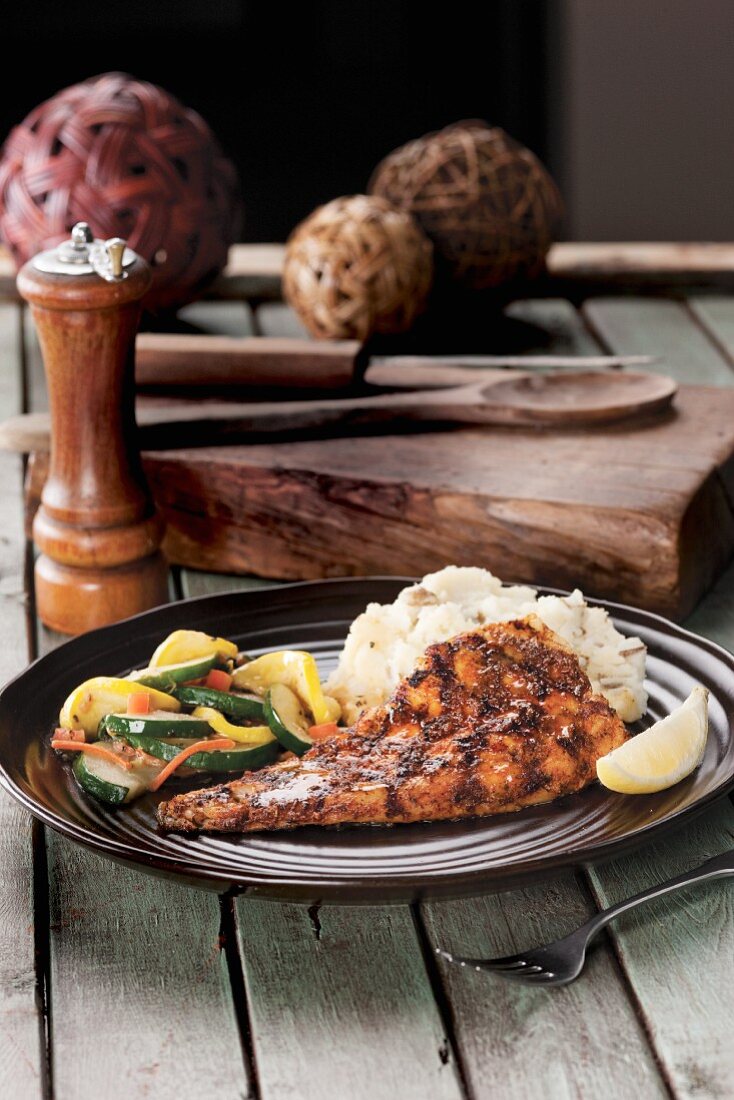 Grilled fish with rice and mixed vegetable shot on wood table with large peppermill