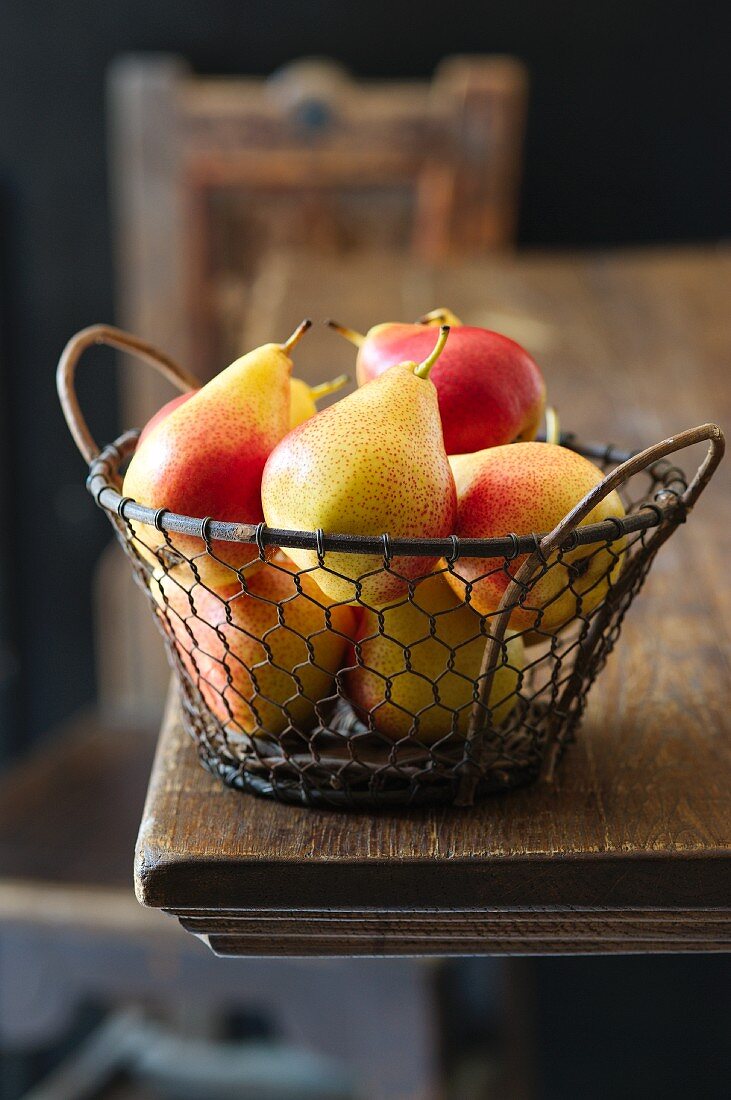 Yellow and red pears in a wire basket on a wooden table