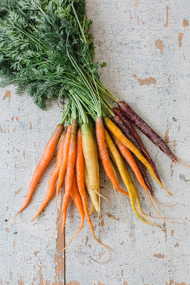 A bunch of fresh colorful carrots on a white wooden background (top view)
