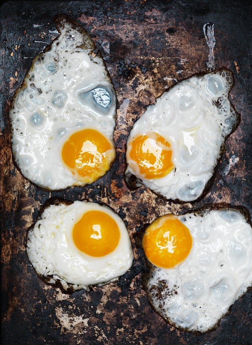 Four fried eggs on a rusty metal plate (top view)