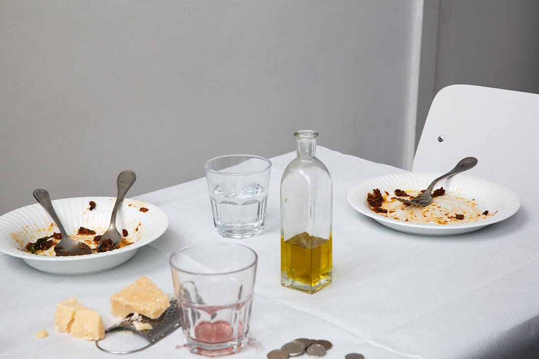 Empty pasta plates, a bottle of olive oil, and blocks of Parmesan on a restaurant table
