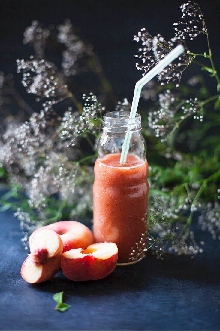 A watermelon and peach smoothie in a glass bottle with a straw