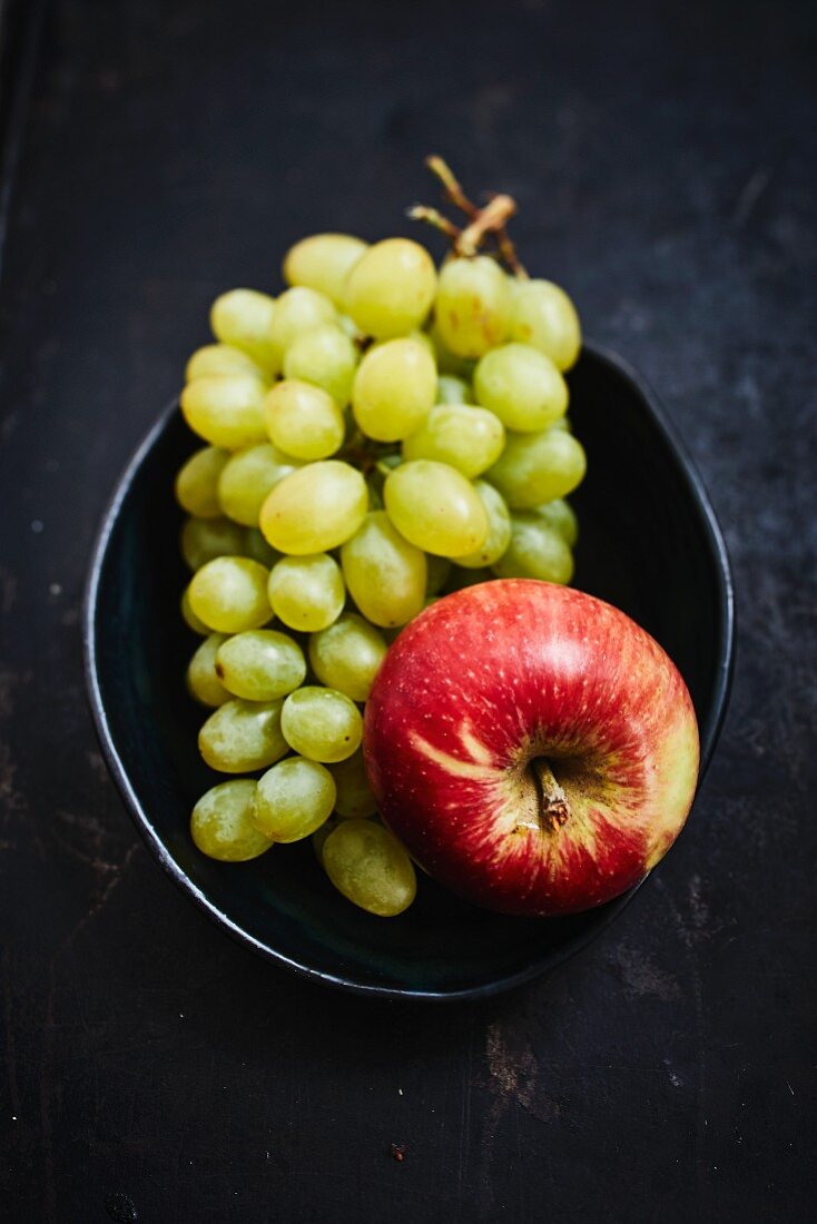 Green grapes and an apple in a bowl on a dark background