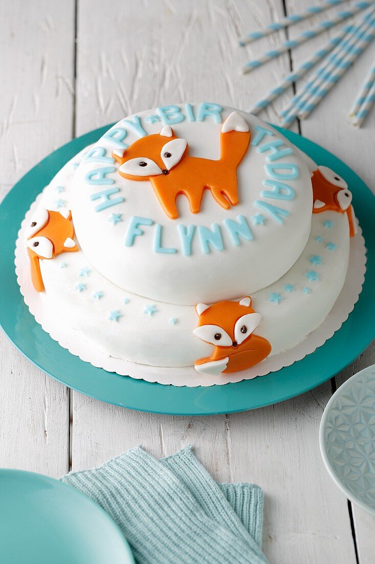 A two tier birthday cake covered with white fondant and orange foxes