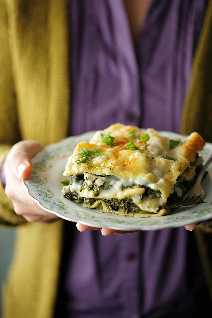 Hände halten Teller mit Spinatlasagne